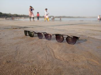 Close-up of sunglasses on sand at beach against sky