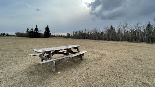 Empty benches and table on field against sky