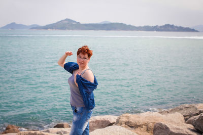 Portrait of woman standing on rock at beach against sky