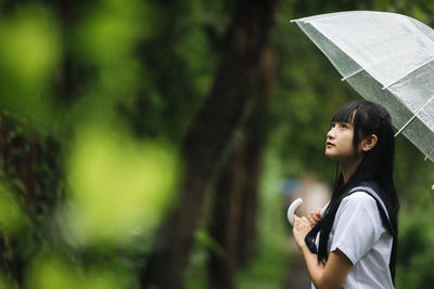 Young student with umbrella standing in park