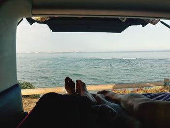 Low section of people relaxing on sea against sky