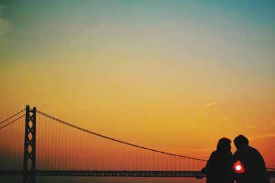 Silhouette couple and akashi kaikyo bridge against sky during sunset