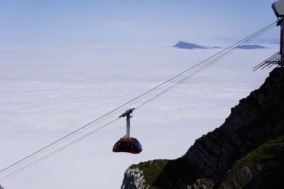 Low angle view of cablecar hanging over clouds against sky