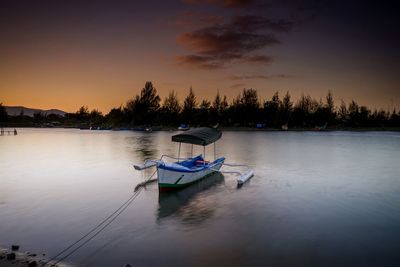 Boat moored in lake against sky during sunset