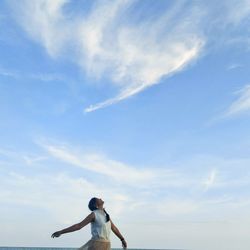 Woman with arms outstretched standing against sky