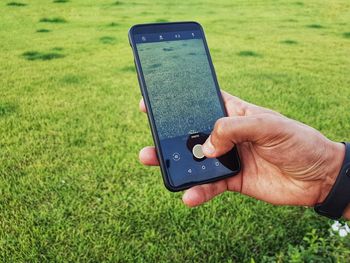 Cropped hand of man photographing grass on mobile phone