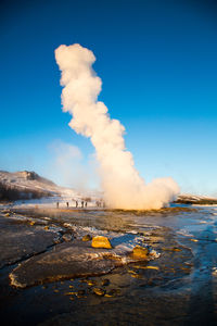 Geyser erupting from volcano landscape against sky