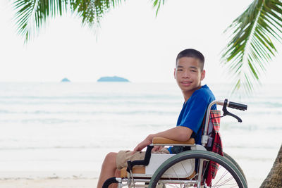 Portrait of boy sitting on wheelchair against sea