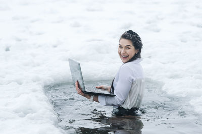 Portrait of young woman sitting on snow covered field