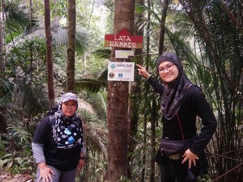 Friends standing by signboard on tree at forest