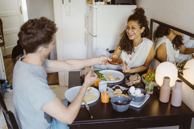 Happy couple sharing food with each other while sitting on dining table at home