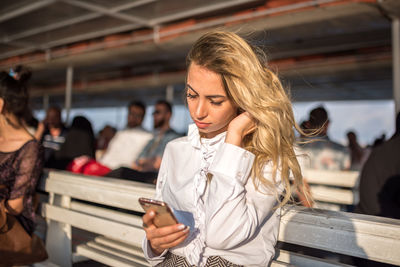 Beautiful young woman using mobile phone while sitting on bench