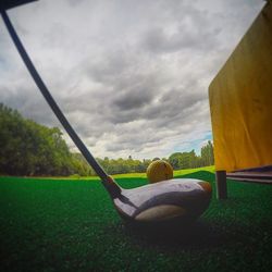 Empty bench on grassy field against cloudy sky