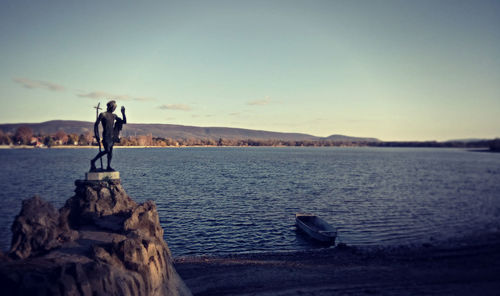 Man standing on rock by sea against clear sky