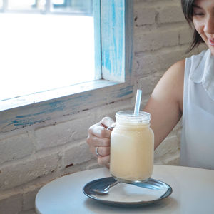Cropped image of woman holding mason jar with drink at table
