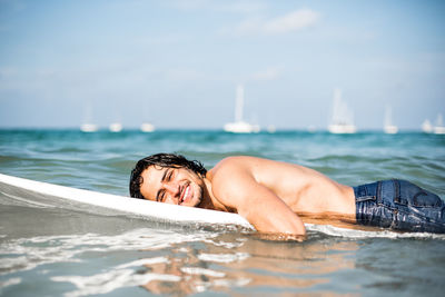 Portrait of shirtless man lying in sea against sky