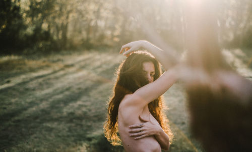 Side view of shirtless woman standing in forest