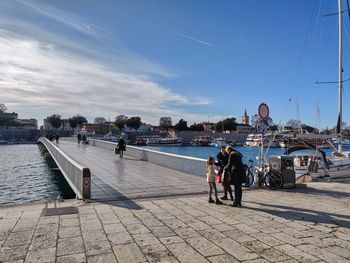 People by river in city against sky