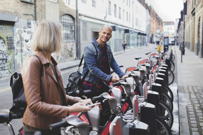 Multi-ethnic couple renting bicycles from bike share stand in city