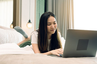 Young woman using mobile phone on bed at home