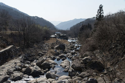 Stream amidst rocks by mountain against sky