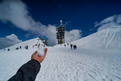 Cropped hand holding snow against sky