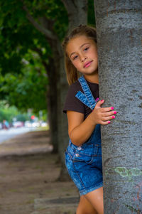 Portrait of smiling girl standing on tree trunk