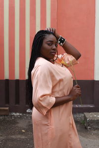 Portrait of young woman standing on road against wall