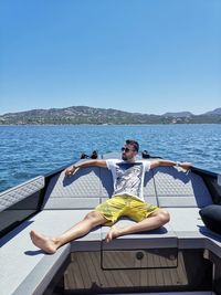 Man relaxing on boat in sea against clear sky