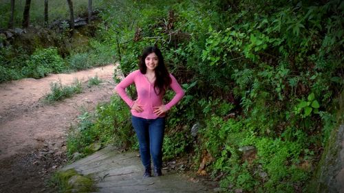 Full length portrait of smiling woman standing on footpath
