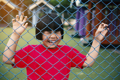 Portrait of young woman seen through chainlink fence