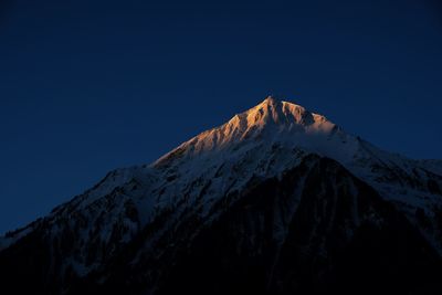 Low angle view of snowcapped mountains against clear blue sky