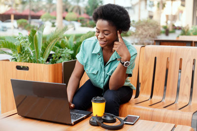 Young woman using laptop while sitting at sidewalk cafe