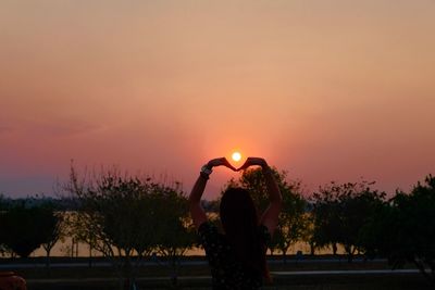 Rear view of silhouette woman with arms raised standing against sky during sunset