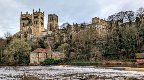 Buildings by river against sky