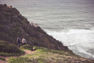 Rear view of hikers walking on mountain against sea