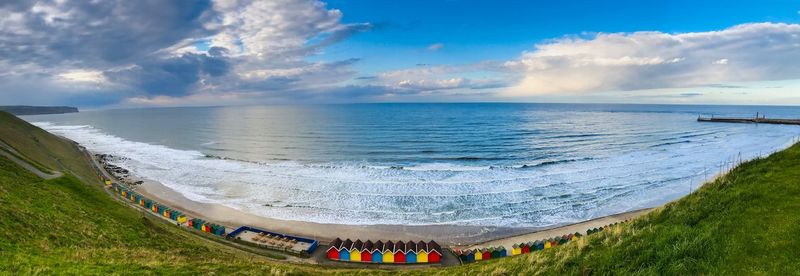 Panoramic view of sea against sky with colourful beach huts in the foreground.