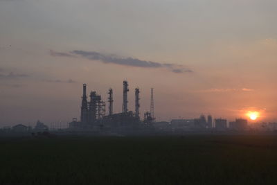 Industry on silhouette landscape against sky during sunset