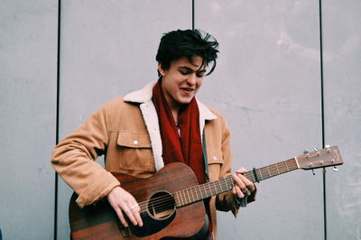 Young man playing guitar against wall