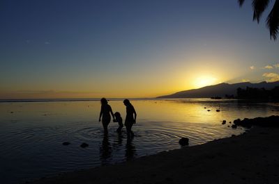 Silhouette people on shore at beach against sky during sunset