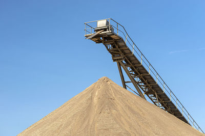 Conveyor belt over heaps of gravel against the blue sky at an industrial cement plant.