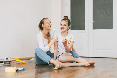 Beautiful and happy mom and daughter paint the walls in the apartment white