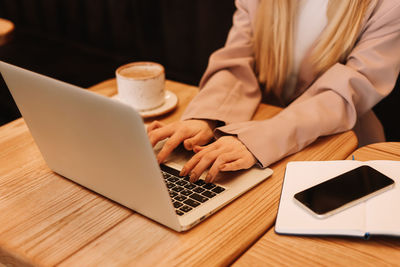 Human hands are typing on a laptop standing on a wooden table. desktop with a coffee mug