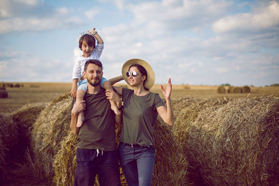 Family mom dad son stand in a sloping field near the haystacks summer