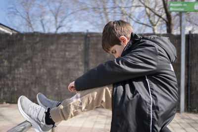 Side view of sad schoolkid sitting with his head down in the street