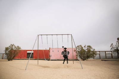 Full length of woman sitting on swing against clear sky