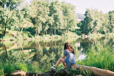 Full length of woman sitting on fallen tree by lake in forest