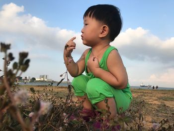 Boy crouching on sand at beach against sky