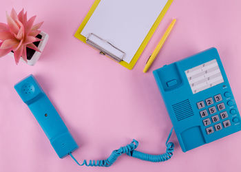 Directly above shot of landline phone with clipboard on pink background