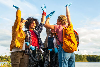 Rear view of friends with arms raised standing against sky